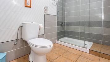 Un baño con inodoro, cabina de ducha de vidrio y piso de baldosas.