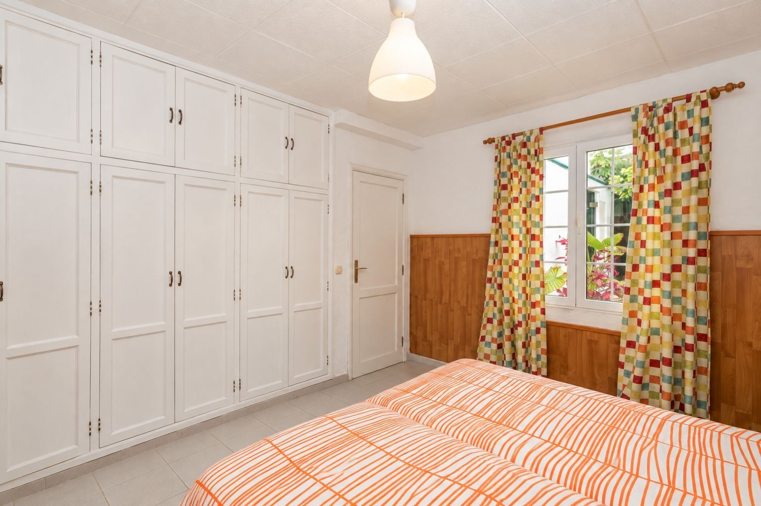 Un dormitorio con cama, armario y ventana con cortinas.