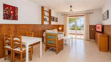 Una habitación con mesa de comedor, sillas, sofá, televisión y un balcón con vistas.