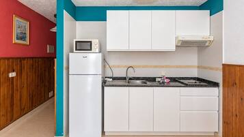 Una cocina compacta con armarios blancos, microondas integrado y pileta de acero inoxidable.