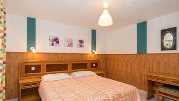 Un dormitorio con cabecera de madera, cama con colcha a rayas anaranjadas, mesita de noche, espejo y lámparas fijadas a la pared.