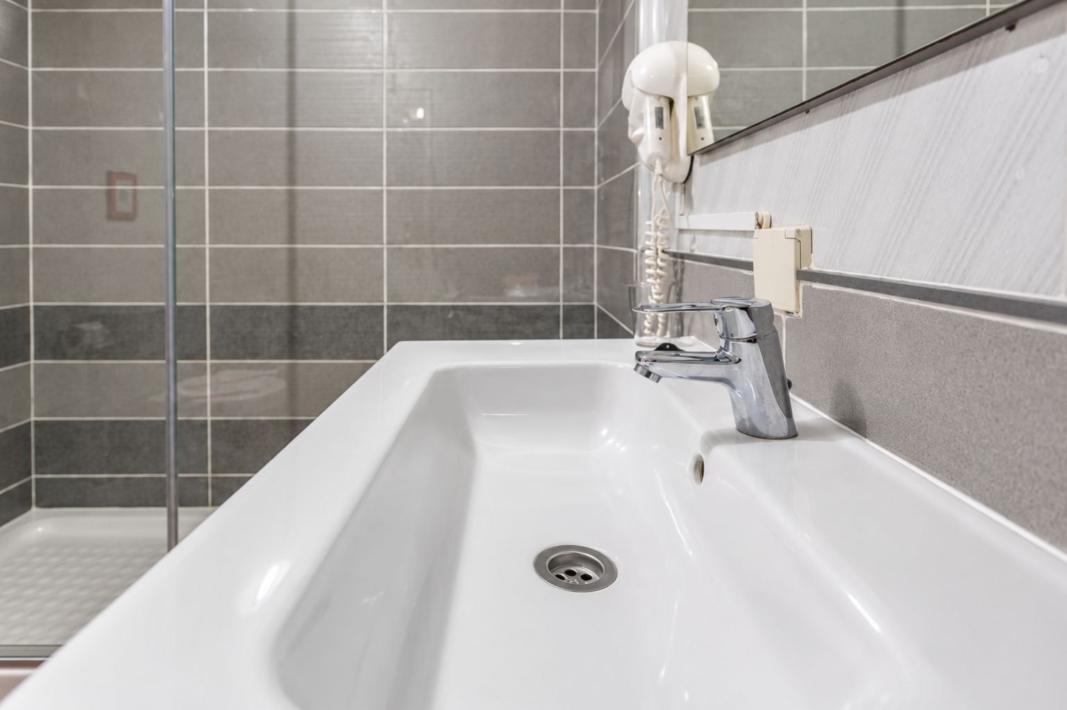 Un baño con un lavamanos blanco, un grifo moderno y un secamanos instalado en la pared.