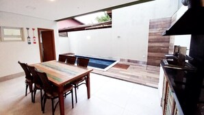 A dining area with a wooden table and chairs, a kitchen with a stove, and a small pool. - House with 3 suites on Juquehy beach. (São Sebastião)