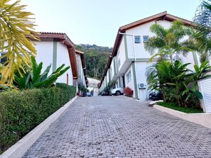 Ein gepflasterter Weg führt zu einem Wohngebiet mit zweistöckigen Gebäuden, umgeben von Grünflächen und einer hügeligen Landschaft.