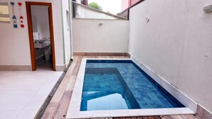 A small swimming pool with a wooden deck, a white wall, and a door leading to a bathroom. - House with 3 suites on Juquehy beach. (São Sebastião)