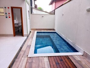 Ein kleiner Pool mit Holzterrasse, einer weißen Wand und einer Tür zu einem Badezimmer.