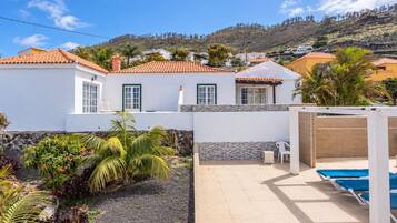 Una propiedad residencial con piscina, jardín con plantas tropicales y vistas a una colina.
