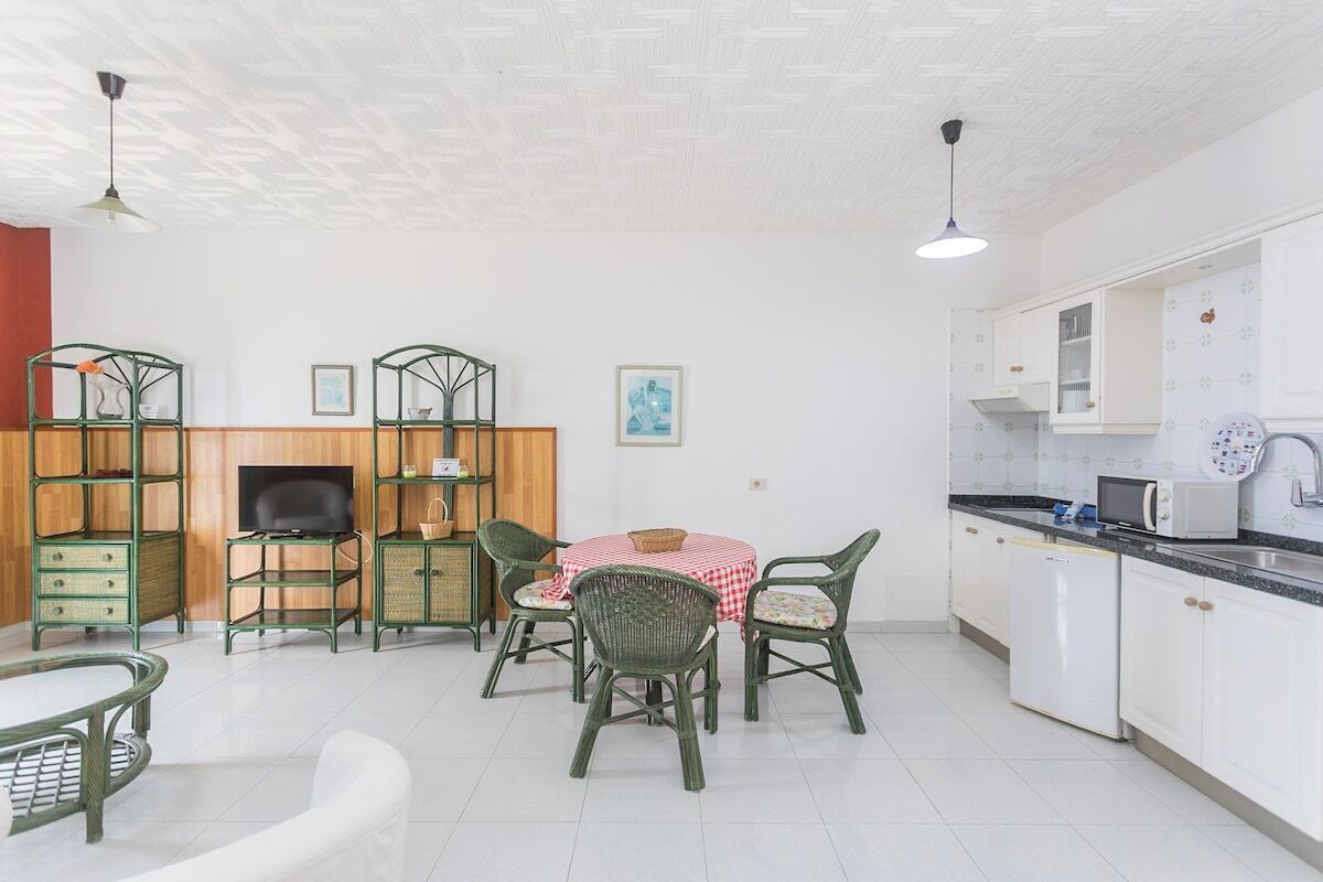 Een keuken met witte kasten, een magnetron, en een eethoek met een tafel en stoelen.