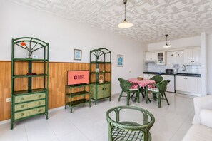 Ein modernes Wohnzimmer mit grünen Möbeln, ein Essbereich mit einer rot-weiß karierten Tischdecke und eine Küche mit weißen Schränken.