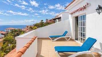 Un balcón con dos tumbonas, suelo de baldosas y vistas al mar y casas vecinas.