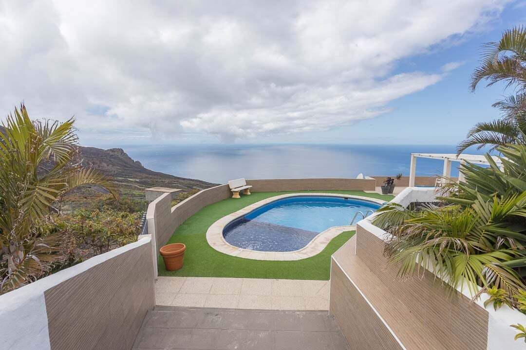 En swimmingpool med en buet kant, omgivet af en lav mur og et lille siddeområde.