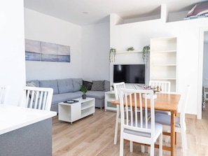 Ein modernes Wohnzimmer mit einer Couch, einem Esstisch mit Stühlen, einem Fernseher und einem Bücherregal.