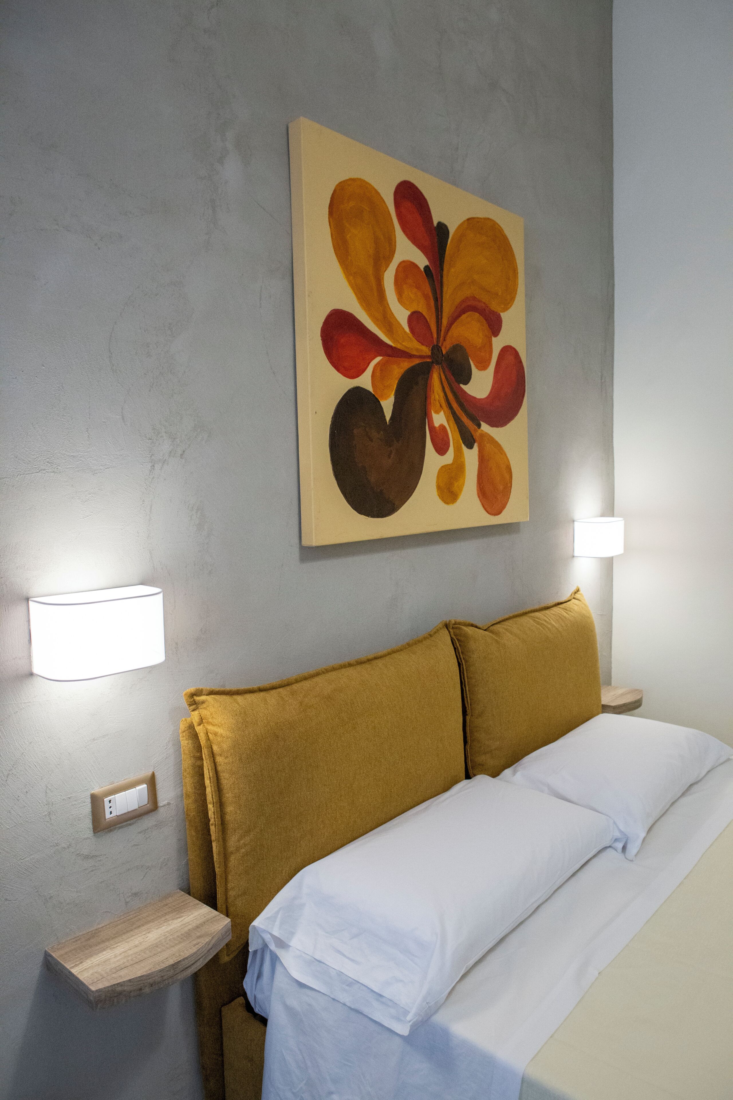 A hotel room with a bed, a wall-mounted painting, and two bedside lamps.