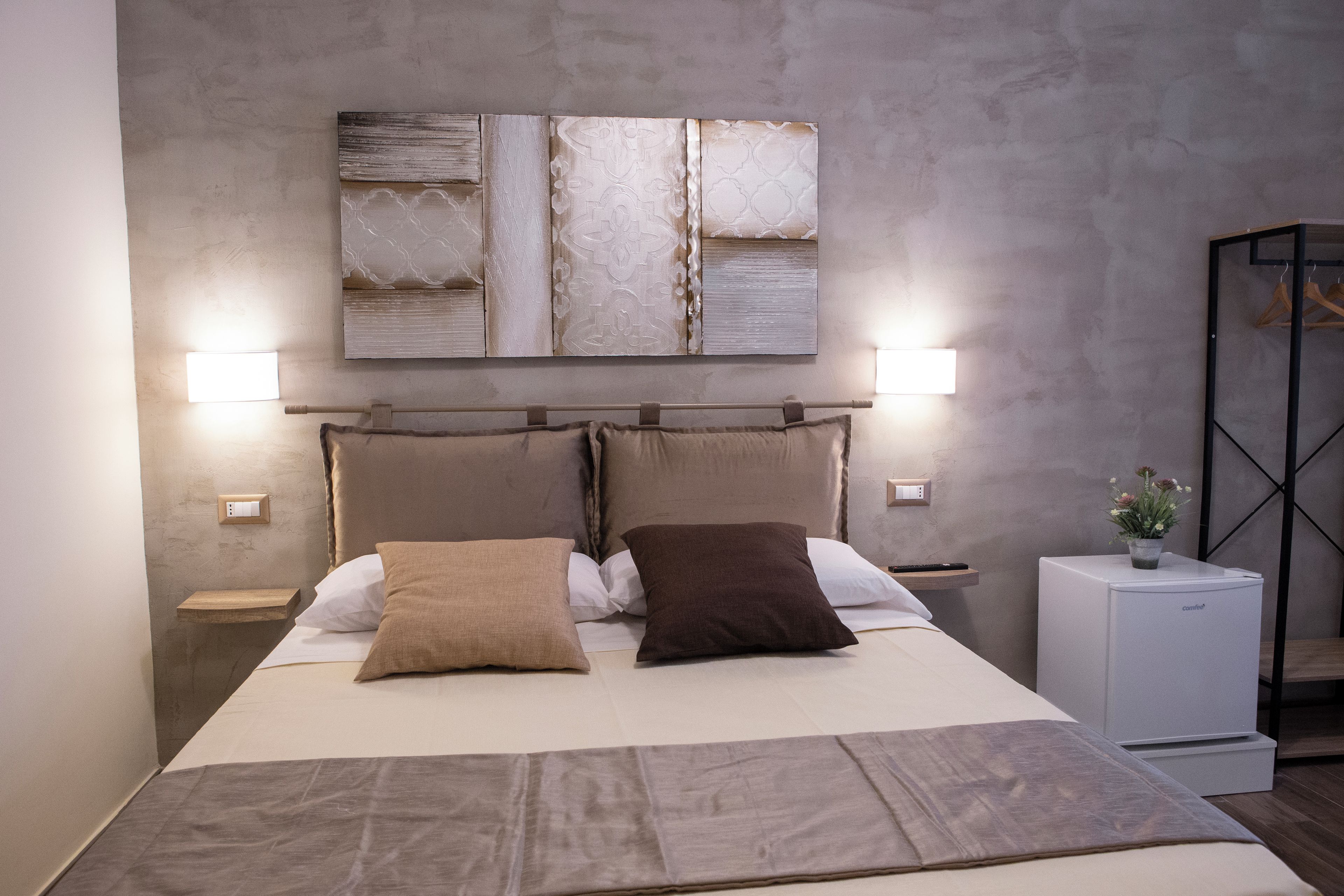 A modern bedroom with a large bed, two bedside tables, a nightstand, a small bedside table with a lamp, and a wardrobe with a mirror.