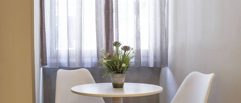 A room with a round table, two chairs, a potted plant, and a window with sheer curtains.