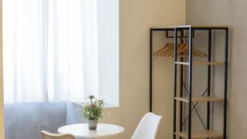 Une pièce comprenant une table ronde, deux chaises, une plante en pot, un climatiseur fixé au mur et une étagère métallique où sont rangés des vêtements.