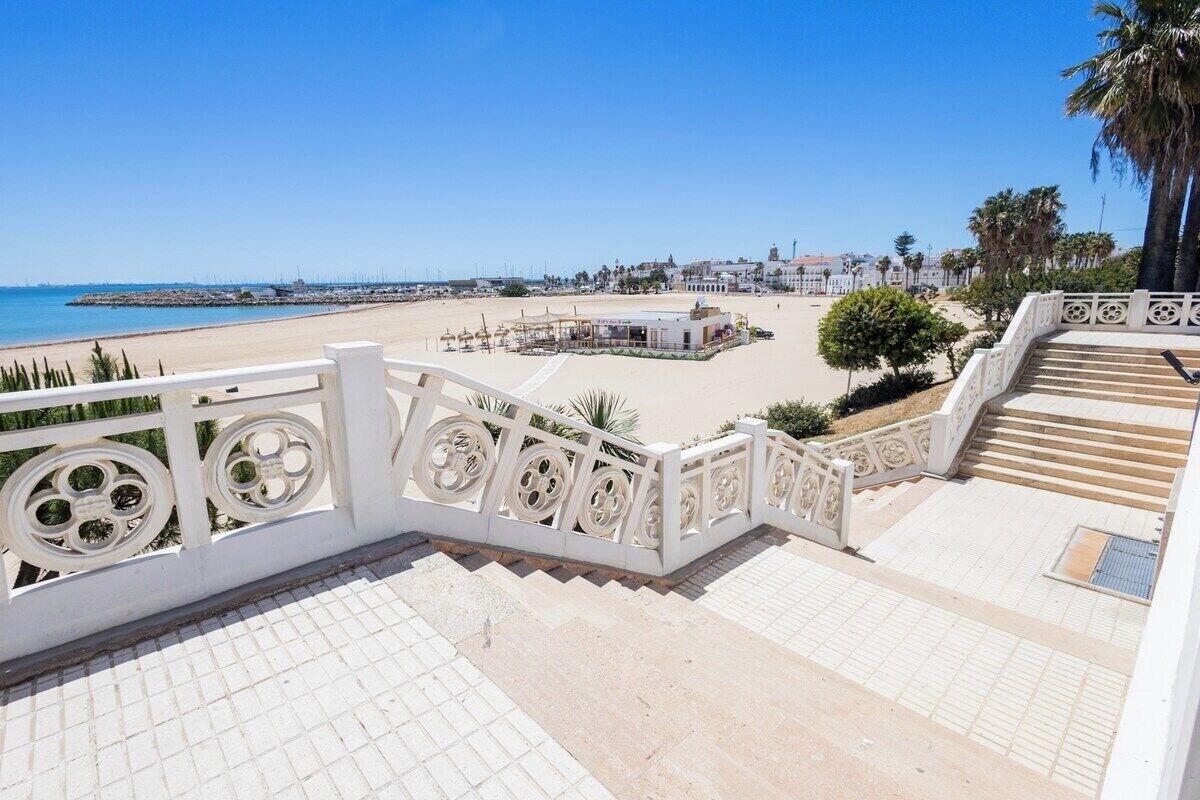 A staircase leading to a beach with a clear view of the sea and a white railing.