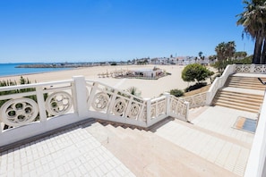 Eine Treppe führt zu einem Strand, mit freiem Blick auf das Meer und einer weißen Brüstung.