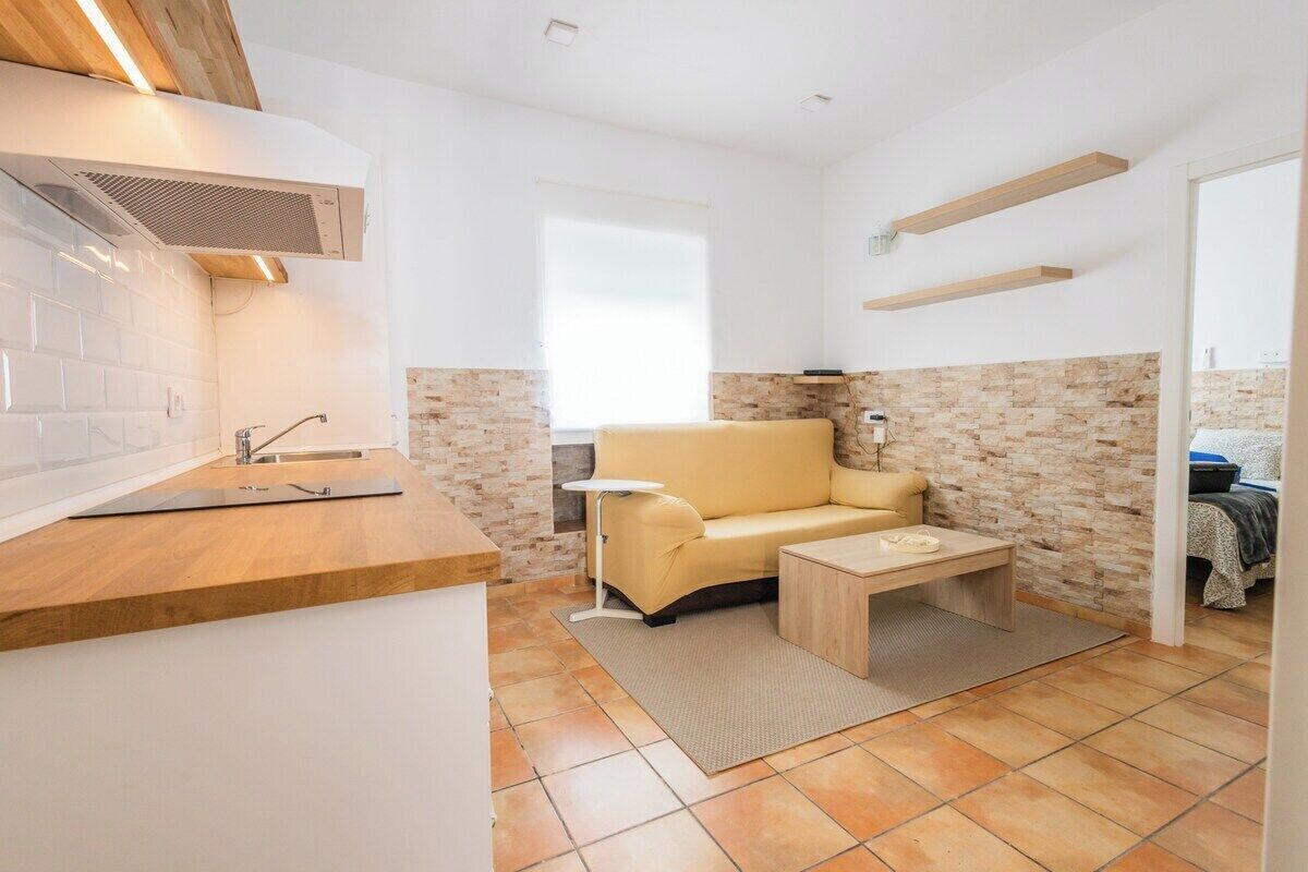 Een compacte leefruimte met een kitchenette, een bank, een eettafeltje en een raam.