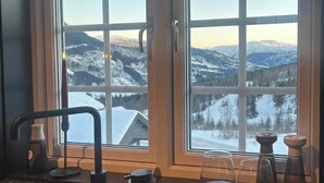 A kitchen with a view of snow-covered mountains, a sink, a plate of cheese and cured meats, and two glasses of red wine.