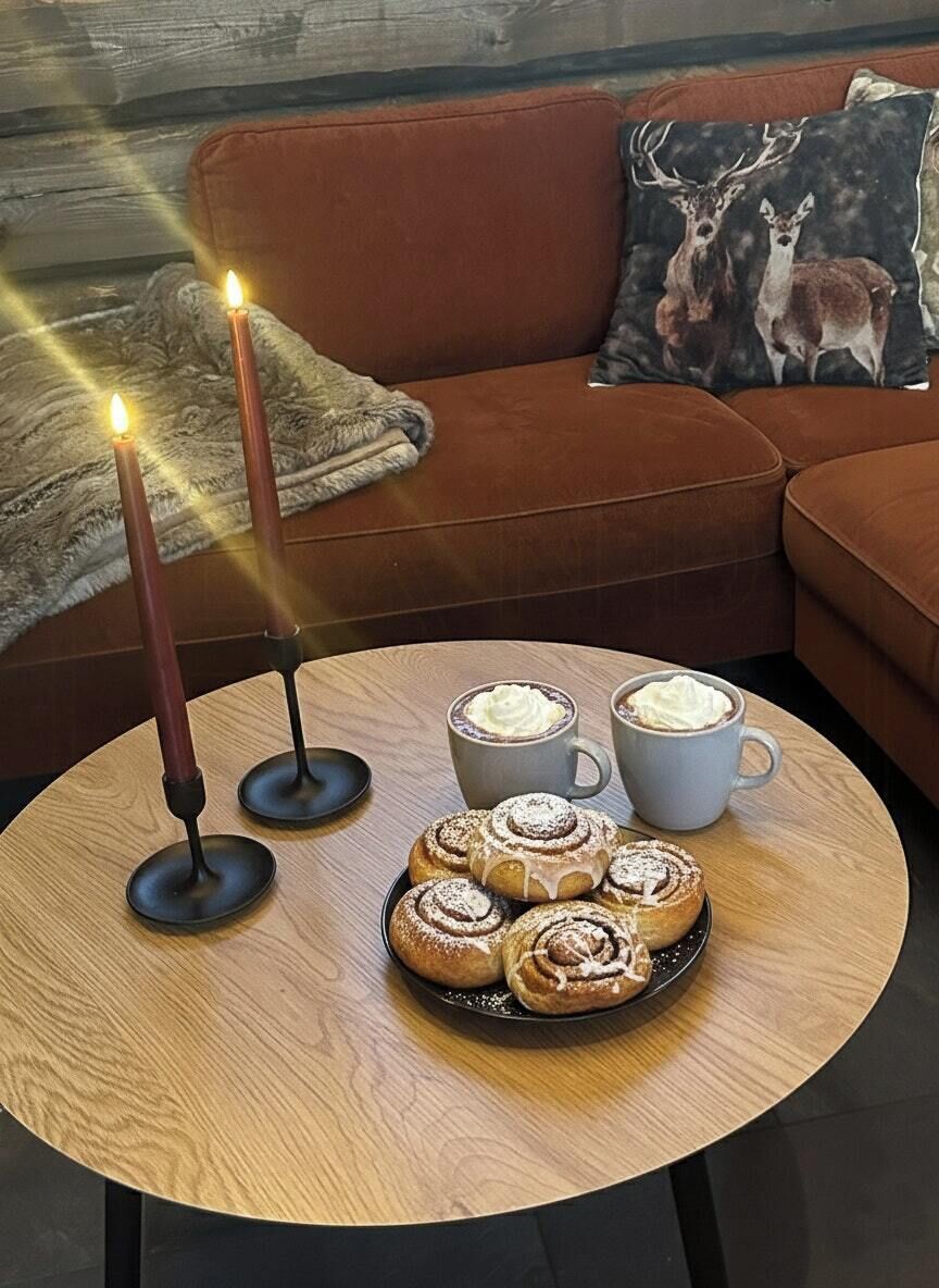 A cozy seating area with a round wooden table, two candles, a plate of pastries, and two cups of coffee.