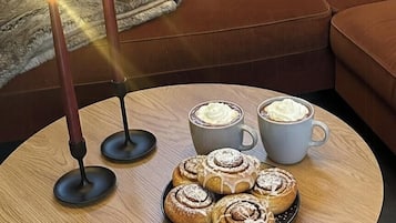 A cozy seating area with a round wooden table, two candles, a plate of pastries, and two cups of coffee.