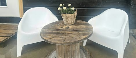 A round wooden table with a woven basket containing white flowers, flanked by two white plastic chairs.