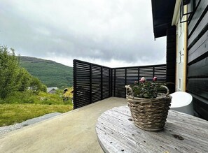 A corner of a building with a black fence, a round wooden table, and a woven basket with a plant.