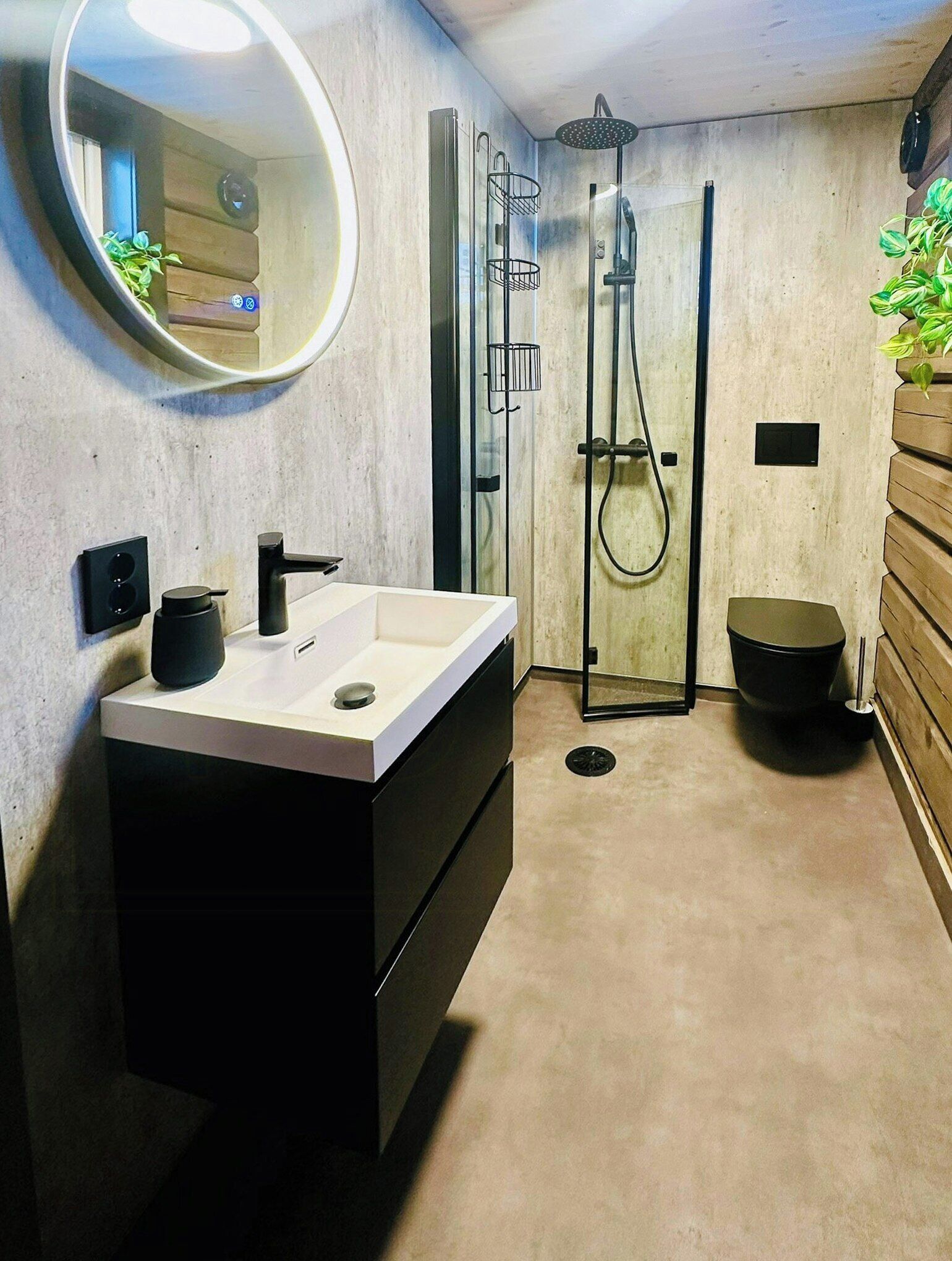 A modern bathroom with a large mirror, a white sink, a black vanity, a glass shower enclosure, and a toilet.