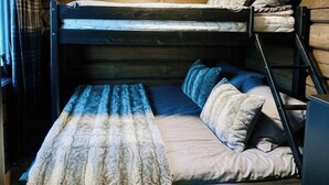 A bunk bed with a blanket and pillows, wooden walls, and a window with curtains.