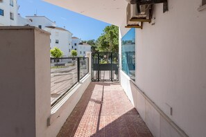 A narrow corridor with a tiled floor, a metal gate, and a view of a residential area with white buildings and trees. - GuestReady - Ancora terraza y piscina (El Puerto de Santa María)
