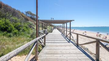 Un paseo marítimo de madera que lleva a una playa con gente y un cielo despejado.