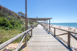 A wooden boardwalk leading to a beach with people and a clear sky. - GuestReady - Ancora terraza y piscina (El Puerto de Santa María)