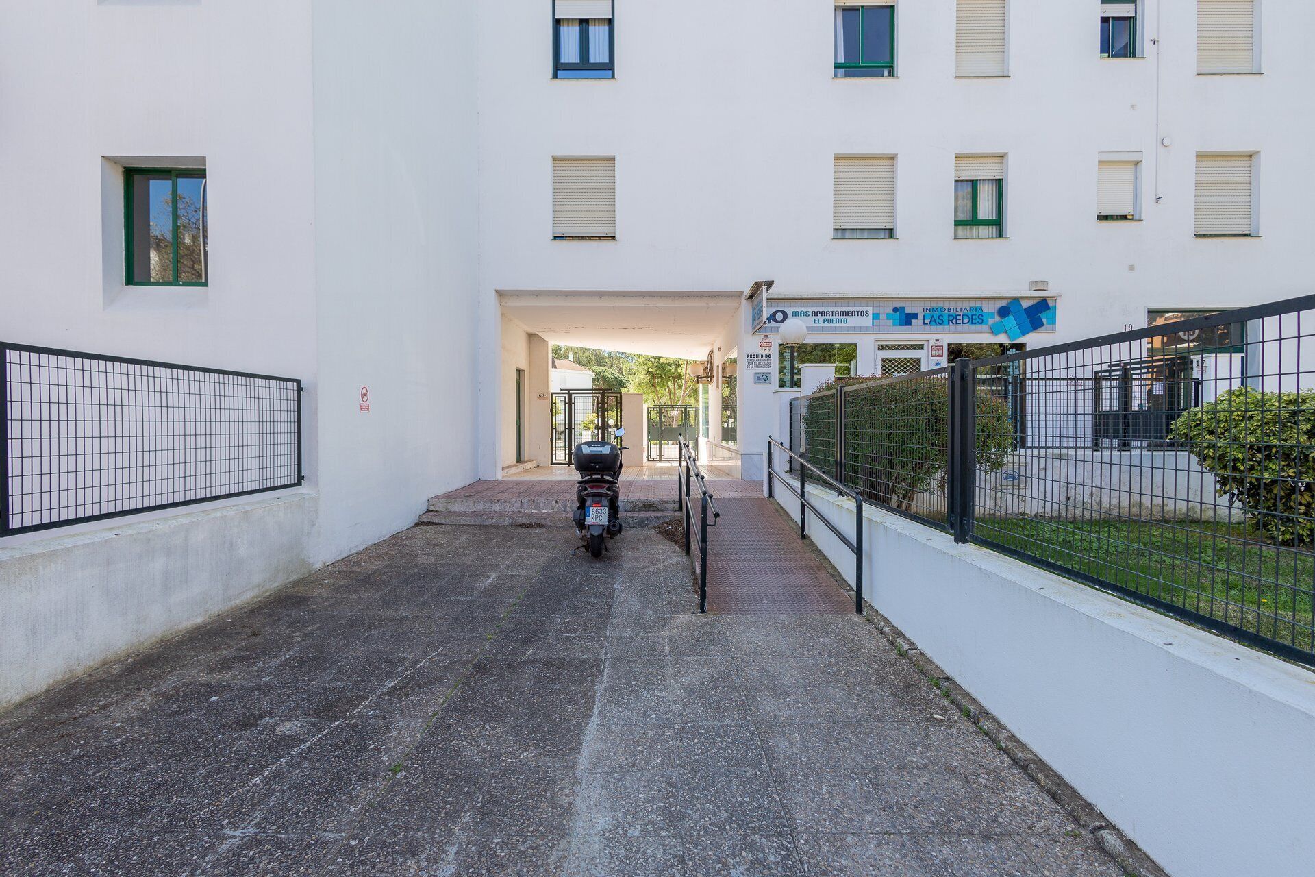 Un estrecho callejón que conduce a una entrada con puerta y una motocicleta estacionada en el centro.