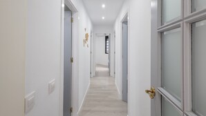 Un pasillo con paredes blancas, puertas de madera con tiradores de latón y piso de madera claro.