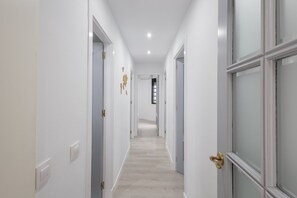 Ein Korridor mit weißen Wänden, Türen mit Messinggriffen und einem hellen Holzboden.