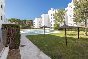 A swimming pool surrounded by a grassy area, with white buildings in the background. - GuestReady - Ancora terraza y piscina (El Puerto de Santa María)