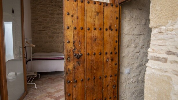 Una habitación con puerta de madera, una cama, una silla y una pequeña mesa.
