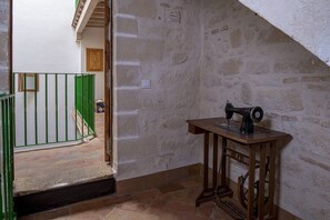 Ein Zimmer mit einer Steinwand, einer Nähmaschine auf einem Holztisch und einem grünen Tor, das in ein weiteres Zimmer führt.