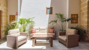 A sunlit patio area with wicker furniture, a wooden table, and potted plants.