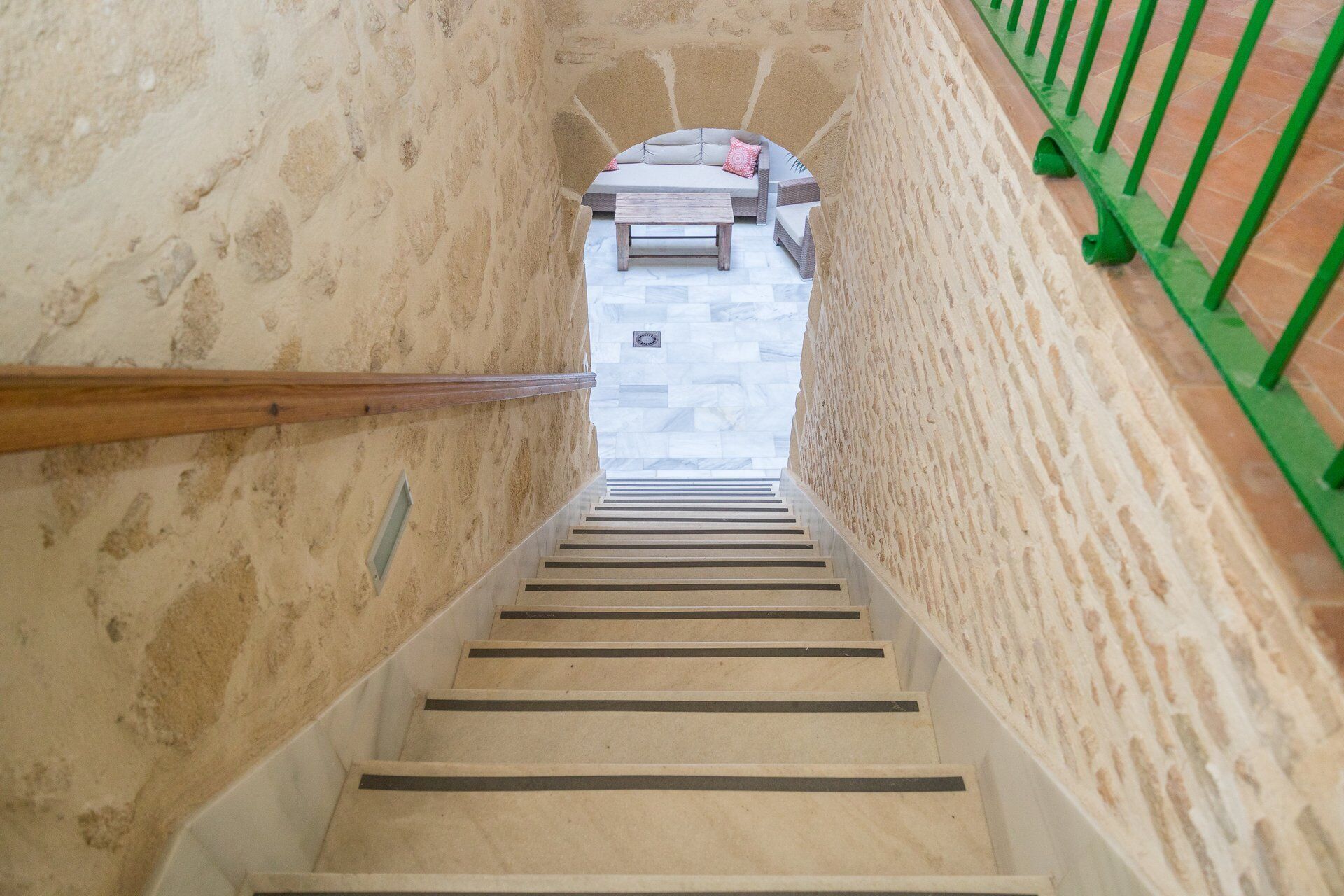 Un escalier avec une rampe en bois menant à un espace détente équipé d’un banc et de coussins.