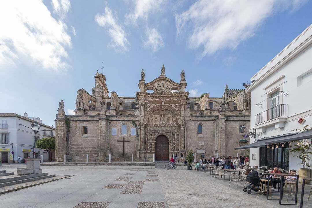 A historic building with a large central doorway, flanked by smaller doors and windows, with a paved plaza in front.