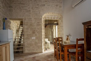 Ein rustikales Interieur mit Steinwänden, einer Holztreppe, einem Essbereich mit Stühlen und Tisch sowie einem weißen Kühlschrank.