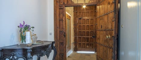Um corredor com porta de madeira, uma mesa com um vaso de flores e piso de azulejos.