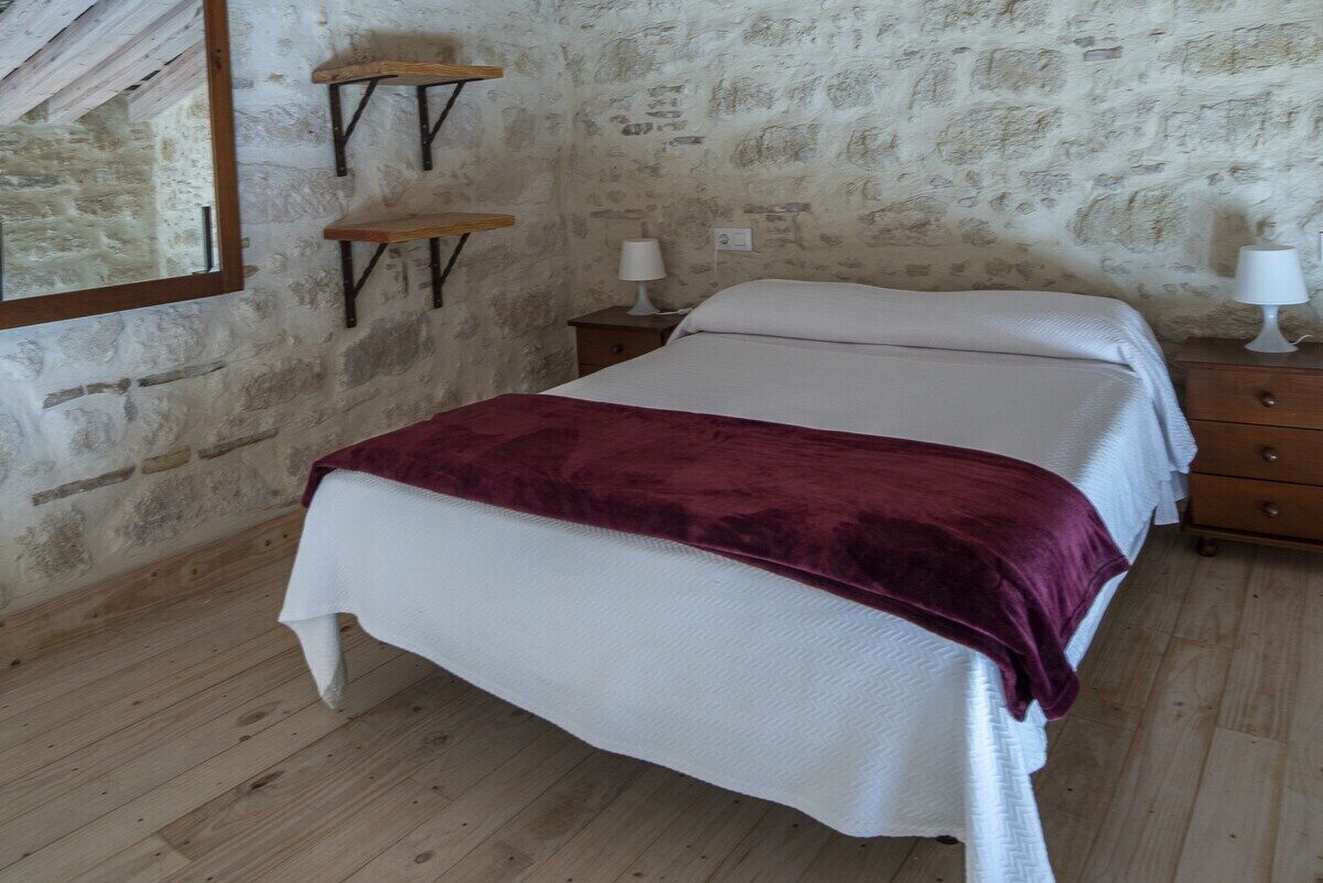 A bedroom with a bed, wooden floor, stone wall, and a mirror.