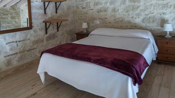 A bedroom with a bed, wooden floor, stone wall, and a mirror.