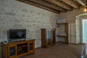 Ein Zimmer mit Steinwand, Holzbalkendecke, einem Fernseher auf einem Holzständer und einer Einbauschränke mit Glastüren.