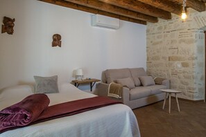 Een slaapkamer met een bed, een bank, een nachtkastje en een stenen muur.