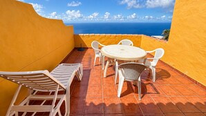 Eine Terrasse mit einem runden Tisch und weißen Stühlen mit Blick auf die Küste.