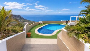 Ein gewundener Pool mit Meerblick, umgeben von viel Grün und einem weißen Gebäude.